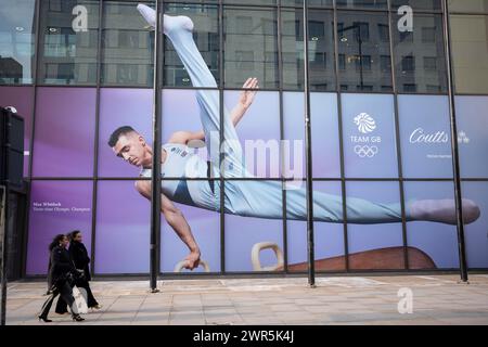 With months before the 2024 Paris Olympics, members of the public pass beneath a huge image of Team GB gymnast and previous Olympic gold medalist, Max Whitlock outside Coutts Bank on the Strand, on 7th March 2024, in London, England. Coutts Bank (and Natwest Bank) are currently Team GB's official corporate partners. Stock Photo