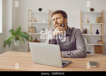 Young male writer sitting at desk with laptop, working on his new book, and thinking Stock Photo