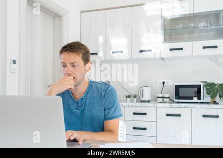 Focused concentrated young businessman work on laptop at home. Serious male professional trader and broker working online on computer with stock Stock Photo