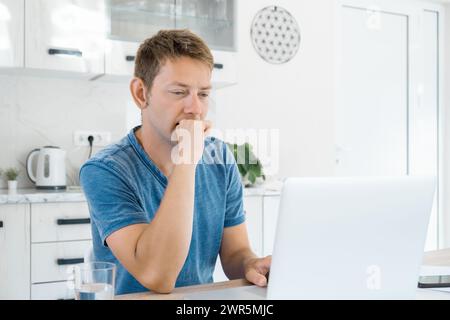 Thoughtfull attractive man working on laptop online at home, using internet. Concentrated male freelancer using computer for distance work. Remote job Stock Photo