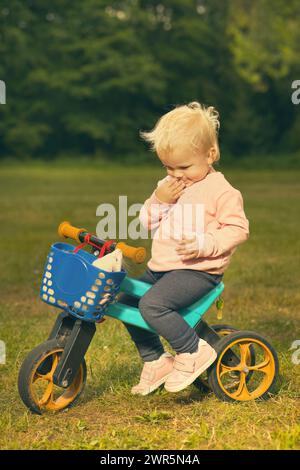 One and half year old baby girl on tricycle bike with ferret friend Stock Photo