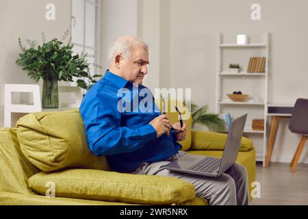 Concentrated senior man sitting on sofa using laptop computer Stock Photo