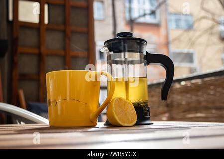 Teapot (French press) with half lemon and teapot at wooden table on the balcony, morning tea time, aromatic aromatherapy fresh and herbal, organic tea Stock Photo