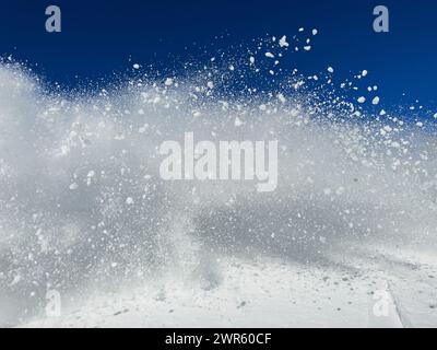 A dynamic explosion of white snowflakes or snow dust against a clear blue sky - abstract contrasted winter background Stock Photo