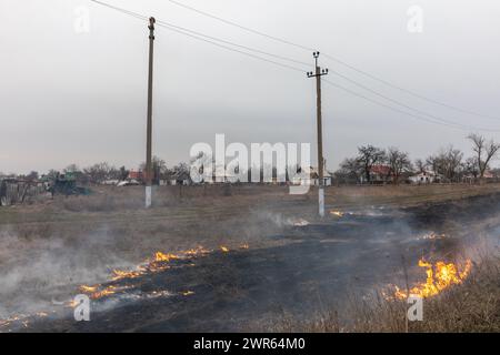 MYKOLAIV Reg, UKRAINE — Mar. 02, 2024: War in Ukraine. Burning grass in the outskirts of a village in Mykolaiv region of Ukraine. Stock Photo