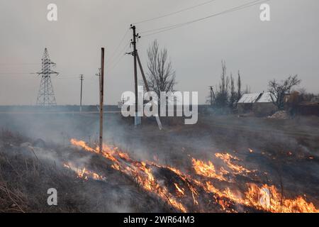 MYKOLAIV Reg, UKRAINE — Mar. 02, 2024: War in Ukraine. Burning grass in the outskirts of a village in Mykolaiv region of Ukraine. Stock Photo