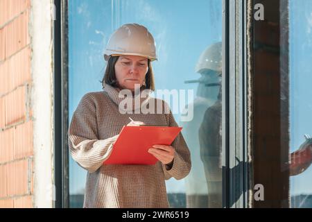 Female architect making notes and remarks during building site inspection, selective focus Stock Photo