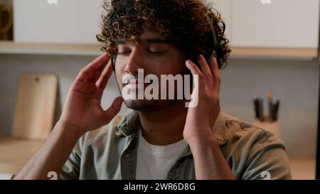 Hispanic man Indian male Arabian guy smiling enjoying high quality sound listening music song audio in modern wireless headphones dancing enjoy Stock Photo