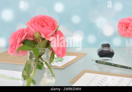 Pink roses in a vase, papers and ink on a glass table. Calligraphy elements. Stock Photo
