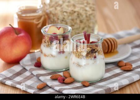 Crunchy granola with yogurt, apple, nuts and honey in glass jars on wooden table. Healthy breakfast concept. Stock Photo