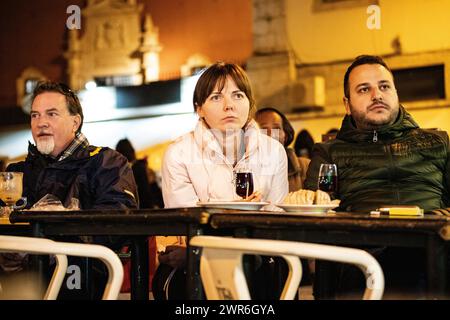 Three individuals engrossed in watching TV at a bar, their expressions a mix of concentration, amusement, and camaraderie Stock Photo