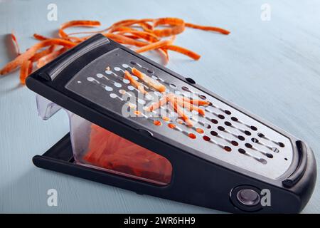 Metal grater and grated shredded carrots on a blue background Stock Photo