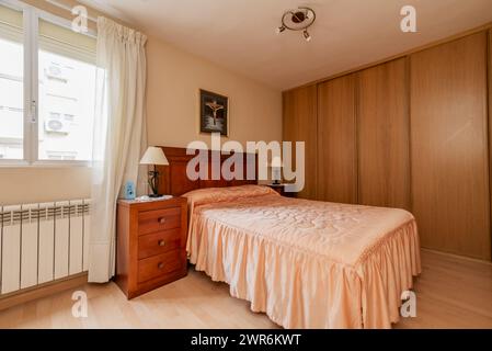 A double bedroom with wooden furniture, a large closet stuck to the wall and an ugly quilt on the bed Stock Photo
