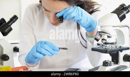 Woman scientist looking through magnifying glass at computer chip near microscope in laboratory Stock Photo