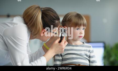 Female pediatrician looking at ear of little girl using otoscope in clinic Stock Photo