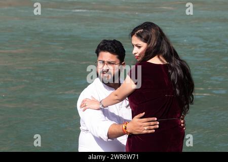 Couple holding each other close against flowing Ganges river water. They are looking away with curious intrigue and a touch of suspicion Stock Photo