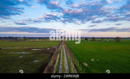 Evening settles over a countryside path cutting through lush fields, with a vibrant sky painting a serene backdrop. Twilight Descends on a Rural Pathway Framed by Pastoral Fields and Sky. High quality photo Stock Photo
