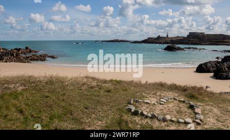 love heart shape of stones in front of Corblets beach Alderney channel Islands golden sandy seashore bay deserted lighthouse in distance Stock Photo