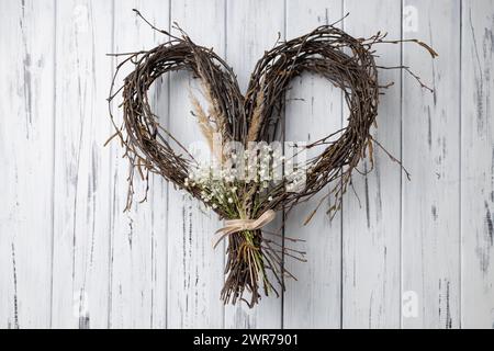 Wicker heart shaped wreath of birch branches hanging on aged wooden wall Stock Photo