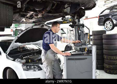 car mechanic maintains a vehicle with the help of a diagnostic computer - modern technology in the car repair shop Stock Photo