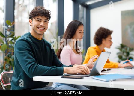 Cheerful latin male student with classmates using laptops Stock Photo