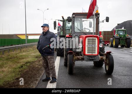 A protesting farmer stands next to a tractor during the blockade of the A2 motorway near Wartkowice in Poland. Following failed negotiation with the Government to reach an agreement, from Monday until Wednesday, farmers decided to block roads in Poland, including the A2 motorway connecting eastern Poland with western Poland. The protest began on Monday morning, traffic on the A2 highway is completely blocked in both directions - Poznan (and the German border), and Warsaw.Farmers have two demands in particular: limiting the inflow of agricultural and food products to Poland from Ukraine and sol Stock Photo