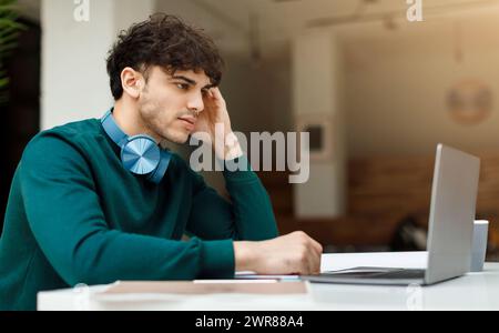 Pensive man student with headphones using laptop Stock Photo