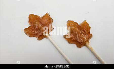 Two maple leave-shaped candies made with brown sugar coating on white sticks, displayed on a table Stock Photo
