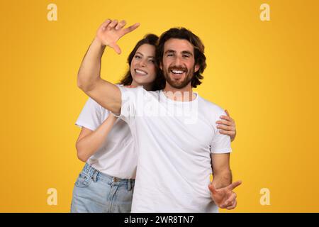 Cheerful young couple playfully gesturing towards the camera, with the woman raising her hand as if capturing a moment Stock Photo