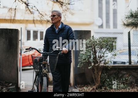 Senior man enjoying a leisurely walk with his bicycle in urban setting. Stock Photo
