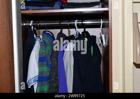 View of outerwear and warm clothes stored on hangers in the closet. Stock Photo