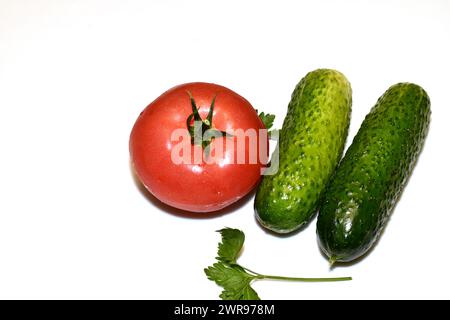 Two ripe cucumbers with a rough green skin and a red tomato with a sprig of greenery lie on a white background. Stock Photo