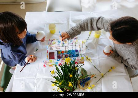 upper view of two children sitting at the table and painting easter eggs Stock Photo