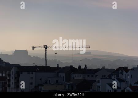 Silhouette of a crane over a city skyline and misty hills at sunset Stock Photo