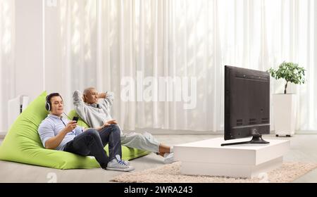 Young men sitting on a beanbags and enjoying in front of tv Stock Photo