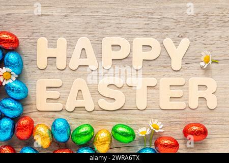 Chocolate, foil covered Easter eggs on wooden background with the text "Happy Easter". Stock Photo