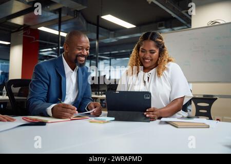 Three happy multiracial colleagues looking down and smiling while using digital tablet in office Stock Photo