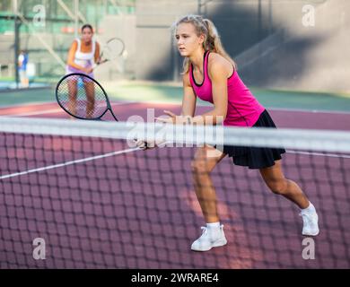 Young forcefully teenage girl playing tennis close to net on court Stock Photo