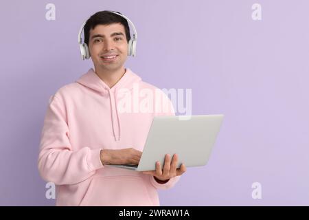Male programmer in headphones working with laptop on lilac background Stock Photo