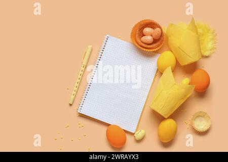 Blank notepad for recipes with pen, Easter eggs and baking molds on orange background Stock Photo