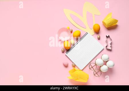Blank notepad for recipes with bunny ears, Easter eggs and baking molds on pink background Stock Photo