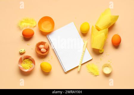 Blank notepad for recipes with pen, Easter eggs and baking molds on orange background Stock Photo