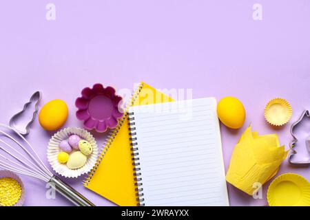 Blank notepads for recipes with Easter eggs and baking tools on lilac background Stock Photo