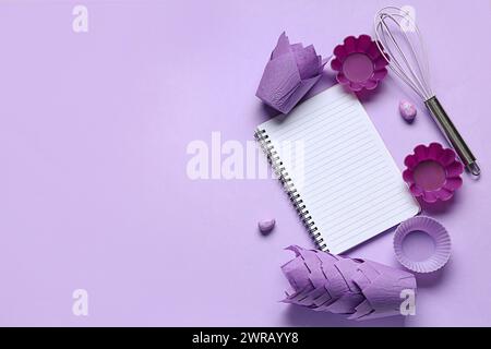 Blank notepad for recipes with whisk, baking molds and Easter eggs on lilac background Stock Photo