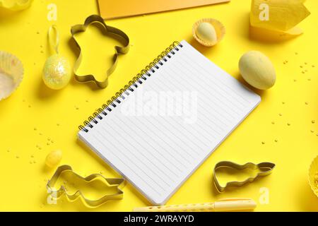 Blank notepad for recipes with pen, Easter eggs and baking tools on yellow background Stock Photo
