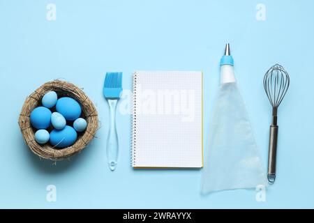 Blank notepad for recipes, baking tools and nest with Easter eggs on blue background Stock Photo