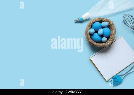 Blank notepad for recipes, baking tools and nest with Easter eggs on blue background Stock Photo