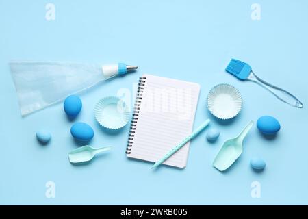 Blank notepad for recipes with pen, baking tools and Easter eggs on blue background Stock Photo