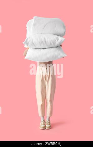 Woman with stack of white pillows and folded blanket on pink background Stock Photo