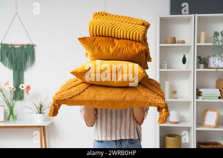 Woman holding stack of pillows with folded warm plaid in room Stock Photo